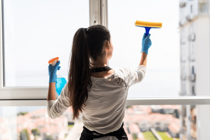 Mujer realizando la limpieza de vidrios en un apartamento.